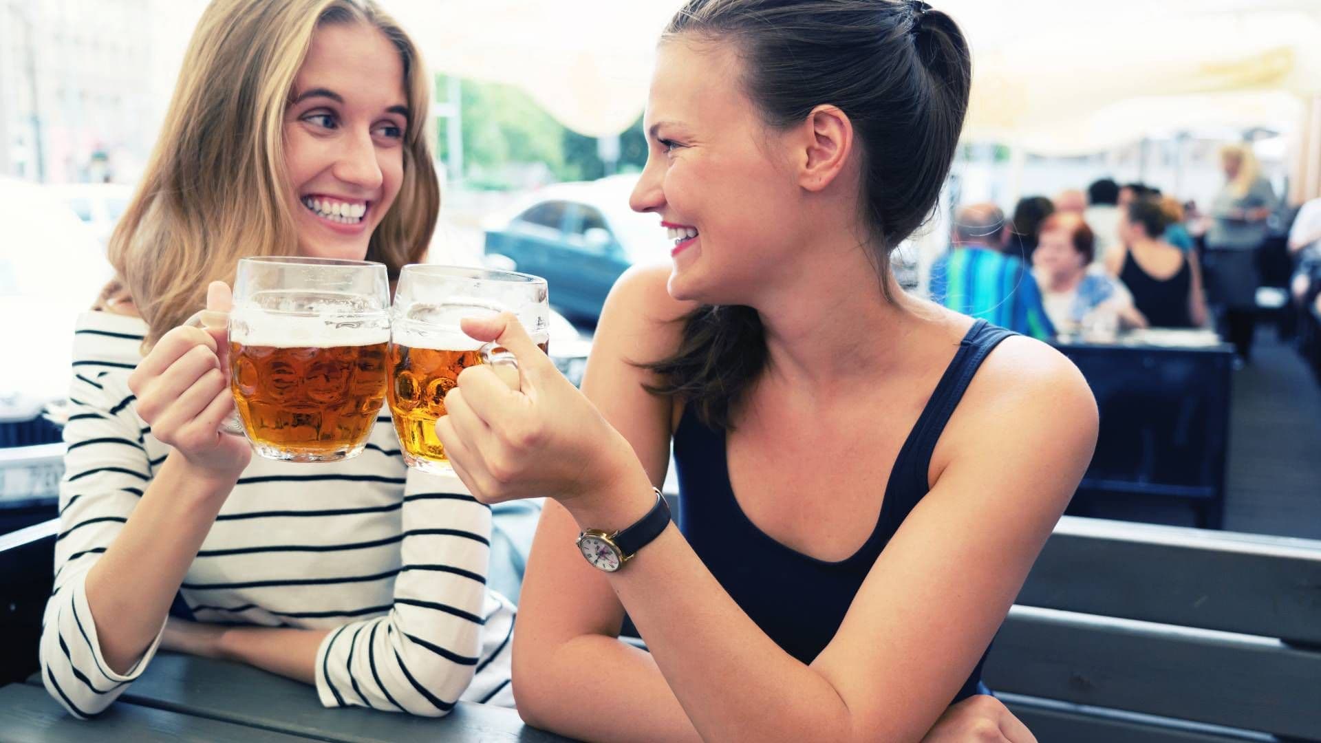 dwie uśmiechnięte kobiety piją piwo na mieście w słoneczny dzień
