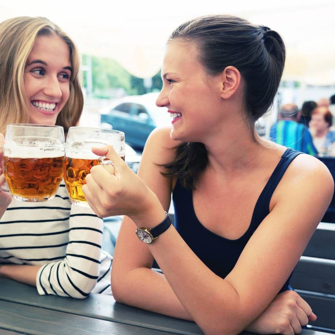 dwie uśmiechnięte kobiety piją piwo na mieście w słoneczny dzień