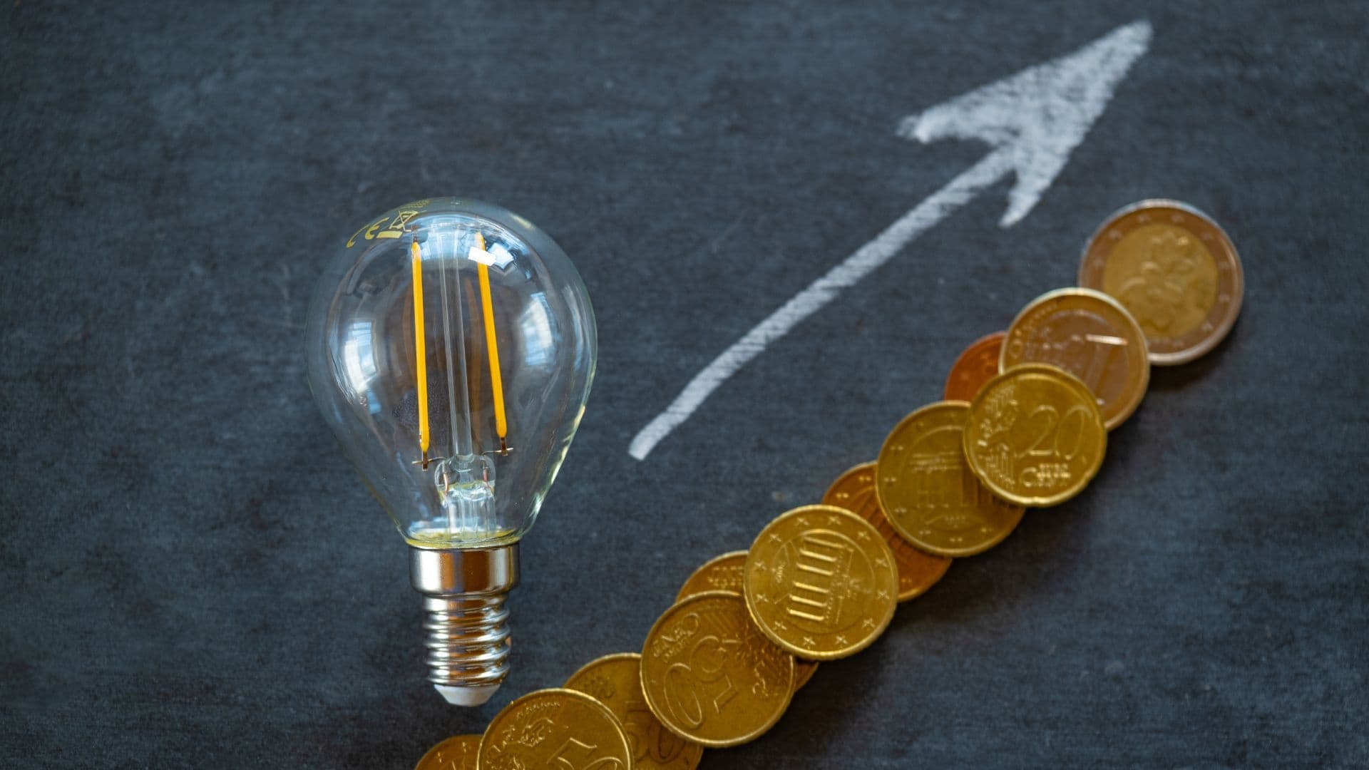 Zdjęcie przedstawia żarówkę, strzałkę w górę oraz monety.
